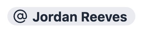 An inserted User Mention chip — a gray pill with the @ symbol before the person's name
